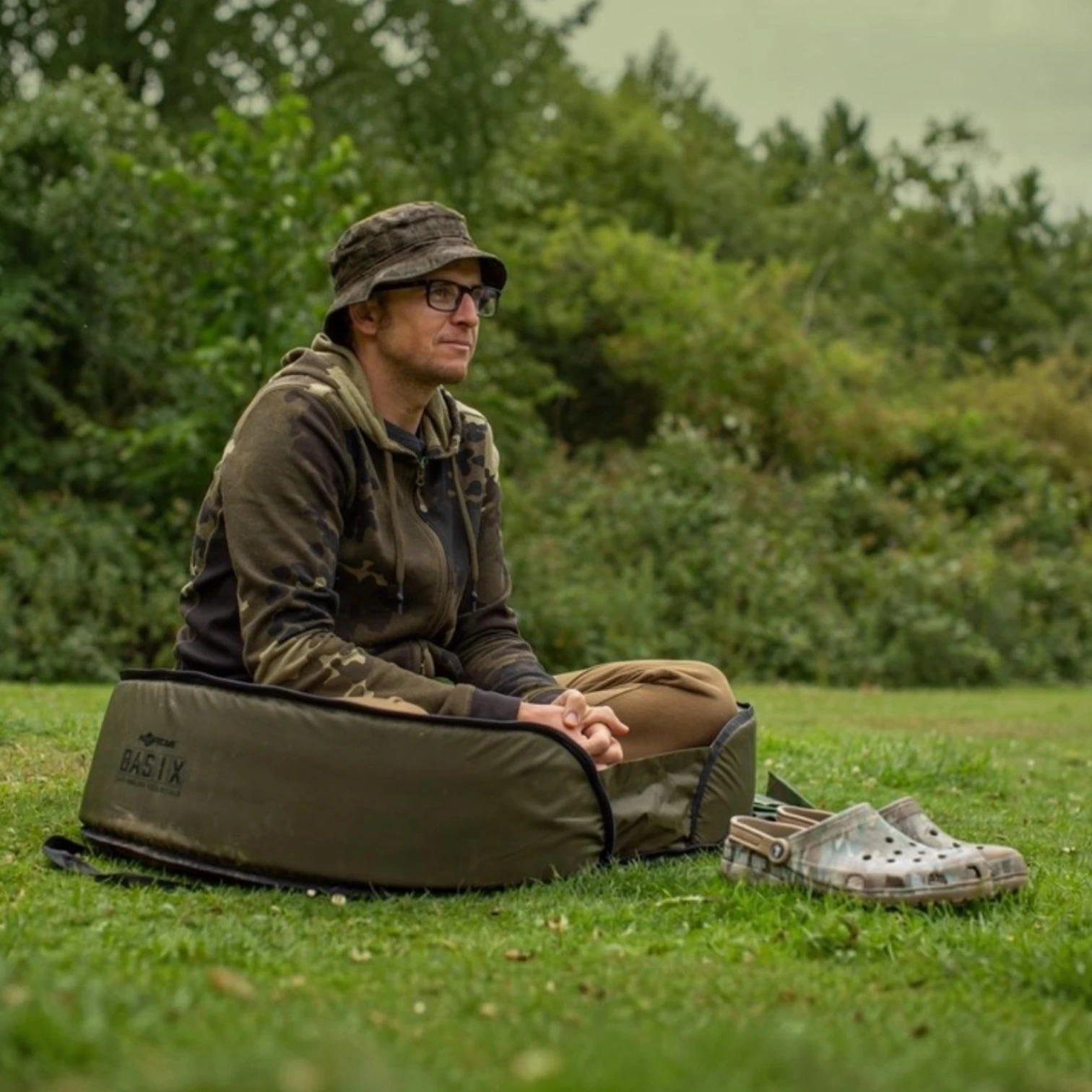 Angler sitting in the Korda BASIX Carp Cradle on a white background.