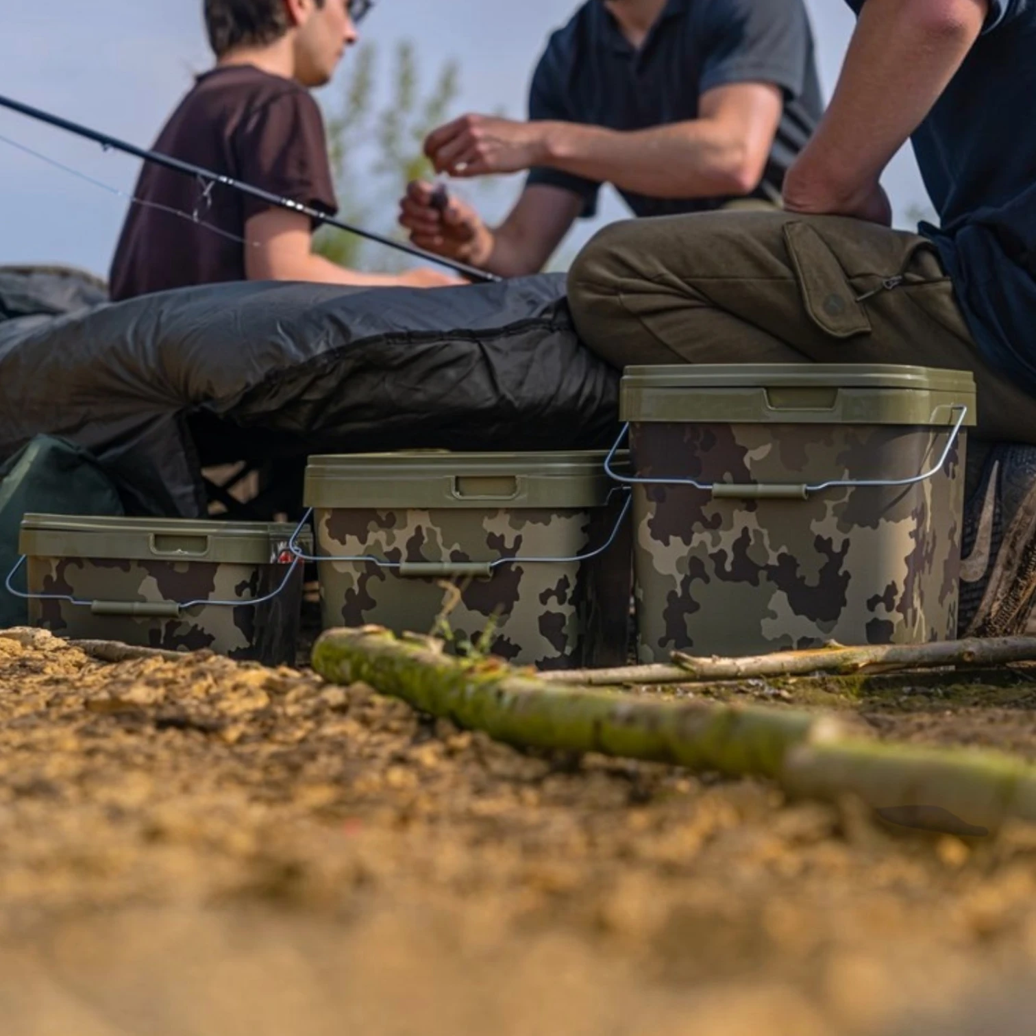 Anglers sitting around during a fishing session with Korda Light Kamo Buckets in the foreground on a white background.
