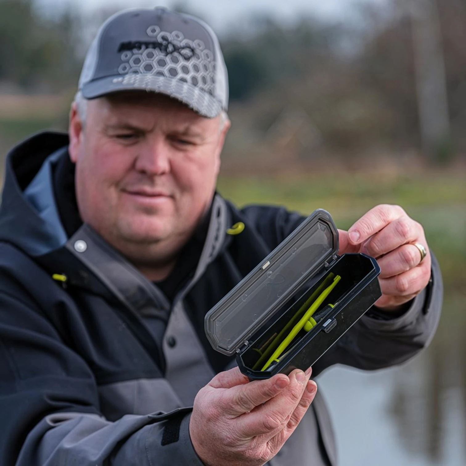 Angler outdoors showing Matrix Slim Accessory Box beside a fishing seatbox on the bank